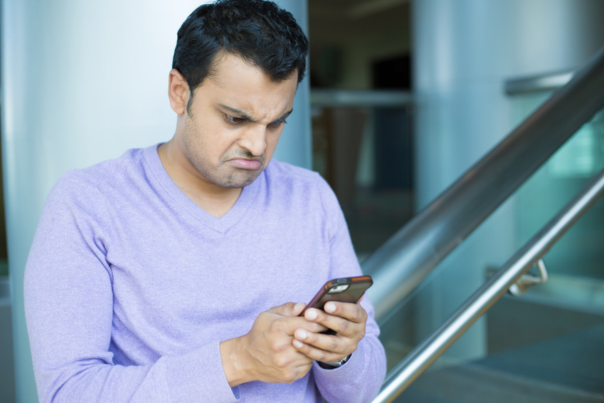 Closeup portrait, stressed young man in purple sweater, shocked surprised, horrified disturbed, by what he sees on his cell phone, isolated indoors office background.